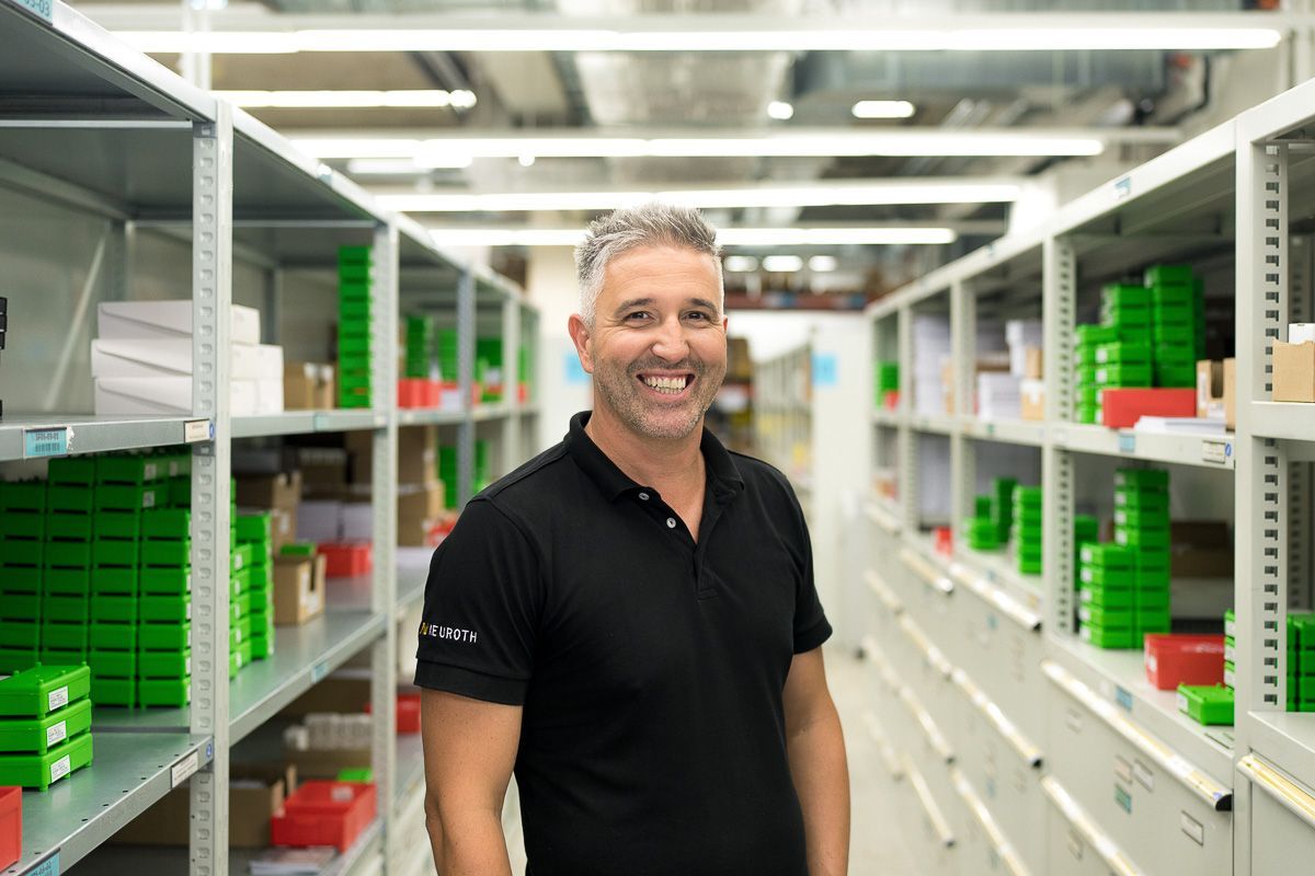 Employe logistique Lebring se tient devant des etageres boites vertes chemise noire